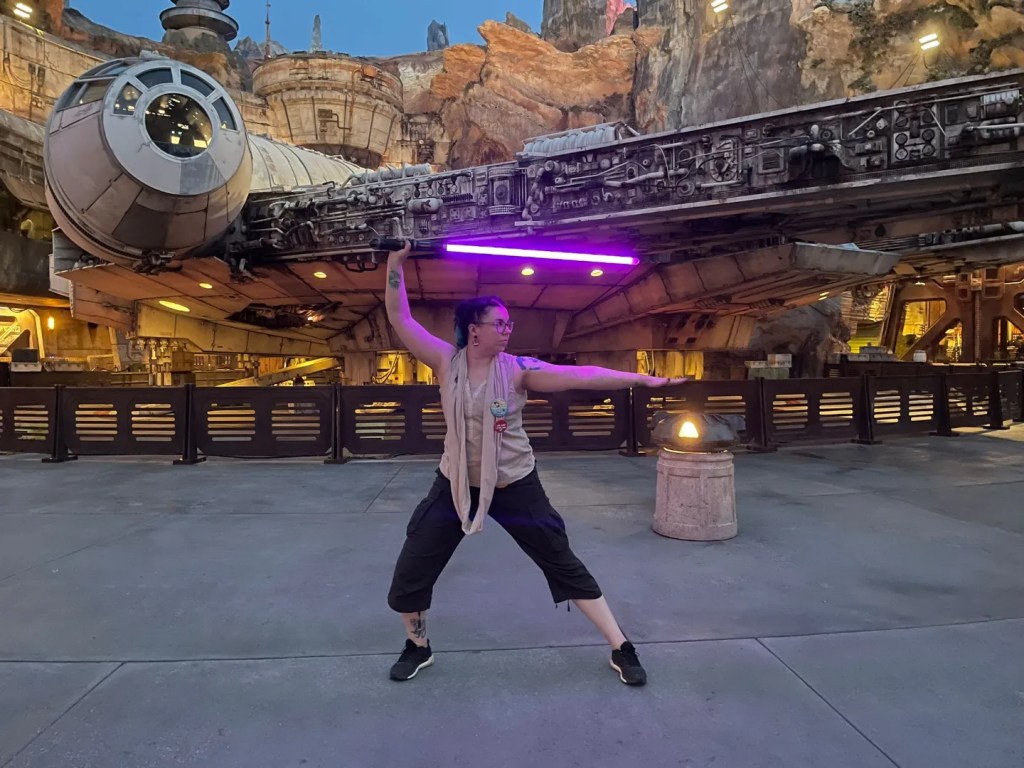 Kokovartalokuvassa Katja poseeraa Millennium Falconin edessä valomiekka päänsä päällä, katse oikeaan reunaan kohti.