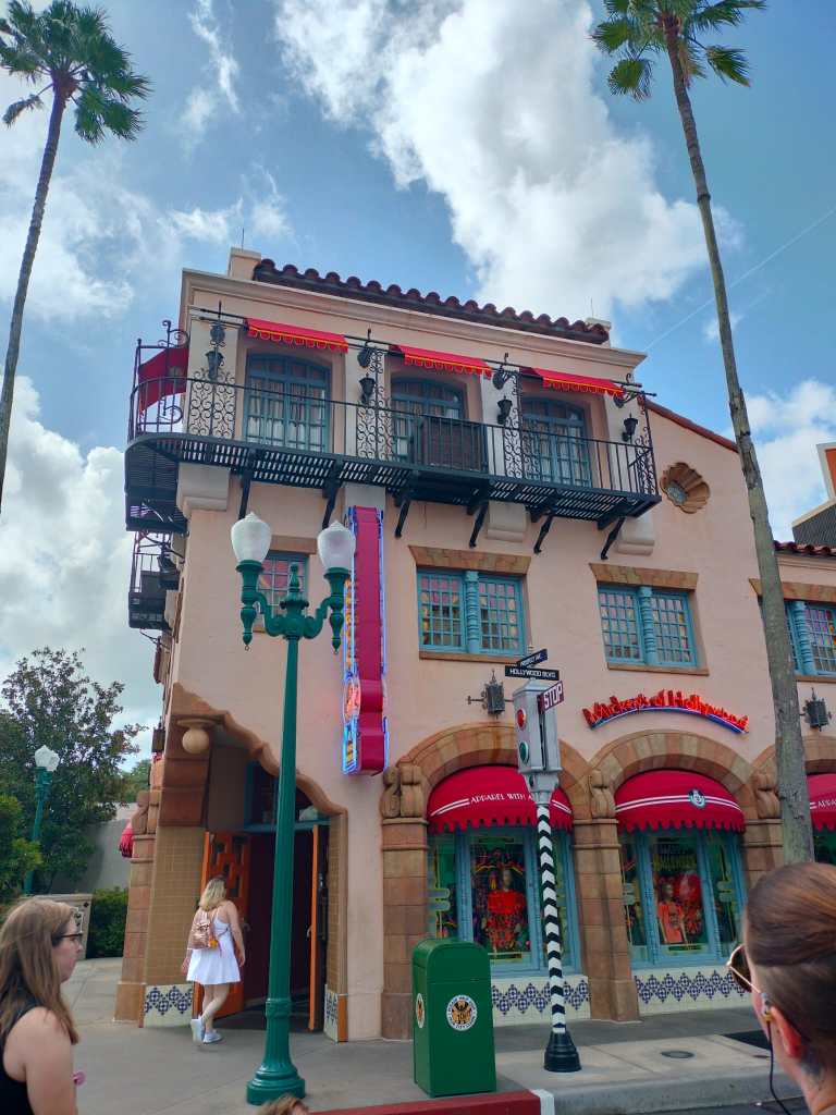 Kuva kadunkulmassa sijaitsevasta vaaleanruskeasta, kolmikerroksisesta rakennuksesta, jossa on vaaleanpunaiset markiisit ja turkoosit ikkunanpuitteet. Ylimmässä kerroksessa on metallinen parveke. Rakennuksesta välittyy kalifornialainen tunnelma.