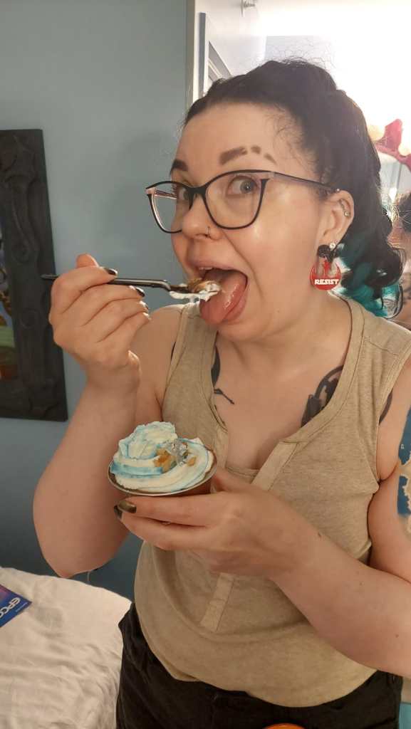 Kuvassa Katja laittaa juuri suuhunsa haarukallista sinivalkoista kuppikakkua. Katjalla on korvissaan kapinaliiton punaiset logot, joissa lukee isolla RESIST.