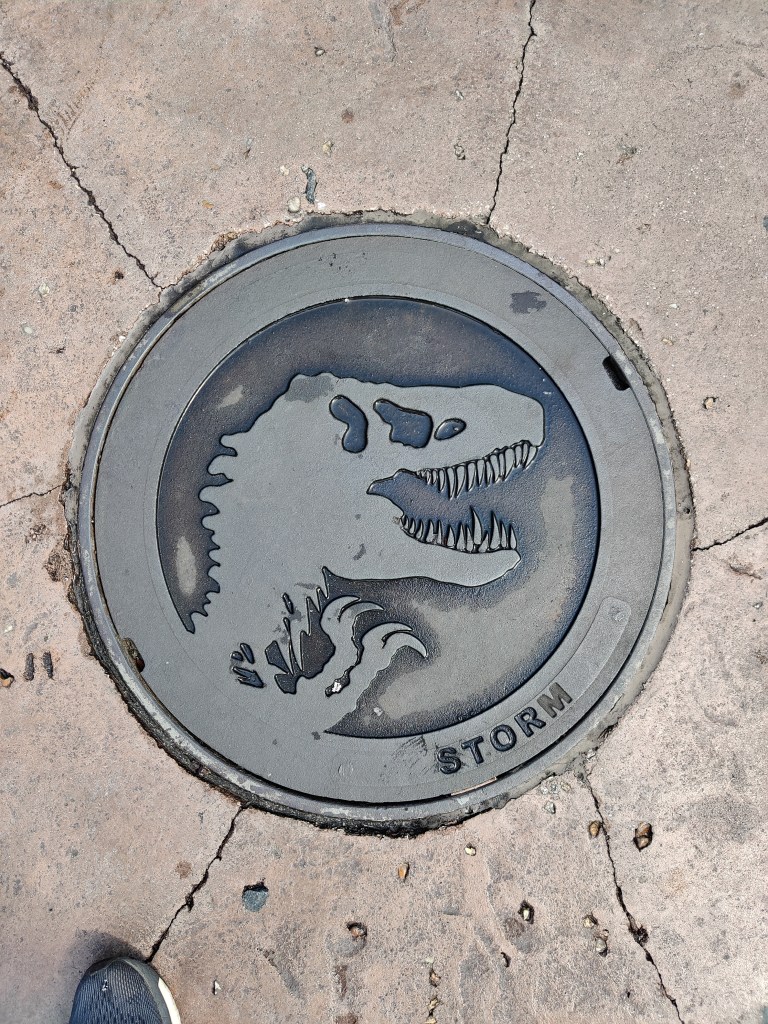 Erikoislähikuva viemäkikannesta, johon on tyylitelty Tyrannosaurus Rexin silhuetti.