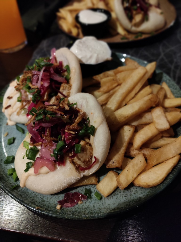 Kuvassa ruoka-annos, jossa kaksi pyöreää taikinakuorta, joissa marinoitua punasipulia, quornia, kevätsipulia ja paahdettua sipulirouhetta. Lisäksi isot ranskalaiset ja dippi.