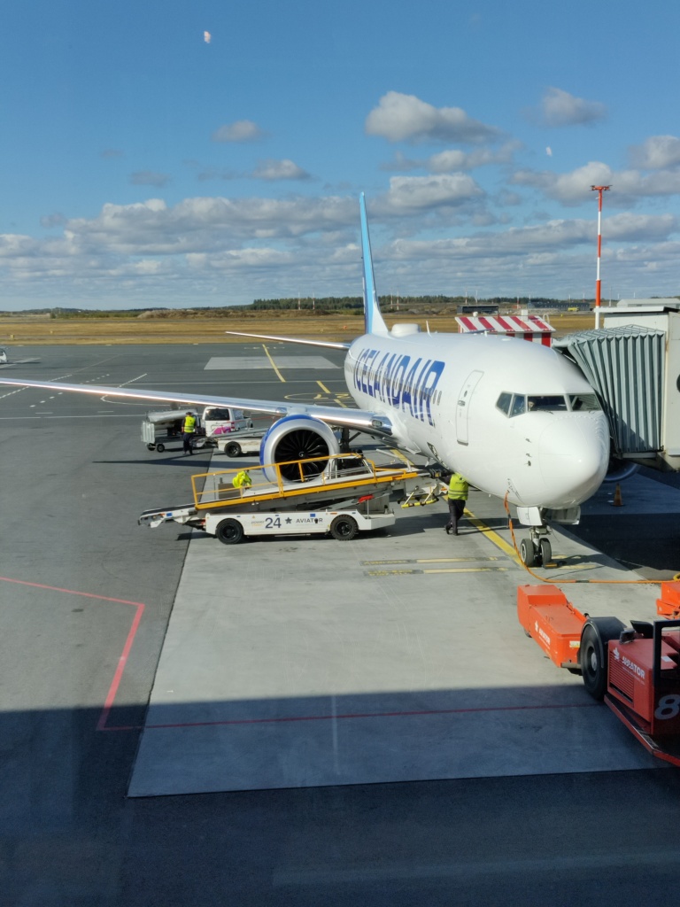 Kuvassa Icelandairin valkoinen lentokone parkissa lentokentällä. Sinne ollaan lastaamassa matkalaukkuja ja muuta tavaraa.