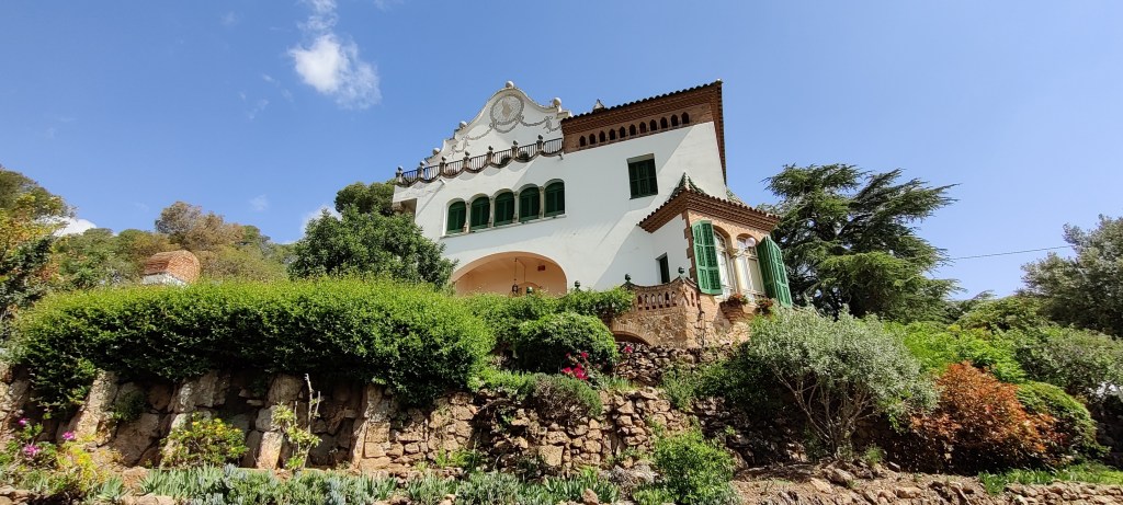 Kivisellä kukkulalla, pusikoiden ja pensaiden keskellä kohoaa valkoinen kivitalo, josta näkyy vihreiden ikkunaluukkujen koristama kulmikas erkkeri, useampi pienempi vihreiden luukkujen peittämä ikkuna ja tasakatto, jolla on jonkinlainen pienen aidan suojaama kattoterassi. Taivas on sininen ja lähes pilvetön.