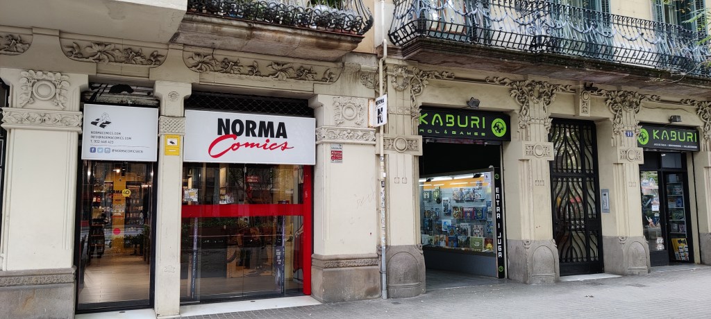 Norma Comicsin ulko-ovi kadun varrella. Vierellä näkyy Kaburi-nimisen pelikaupan ovet.
