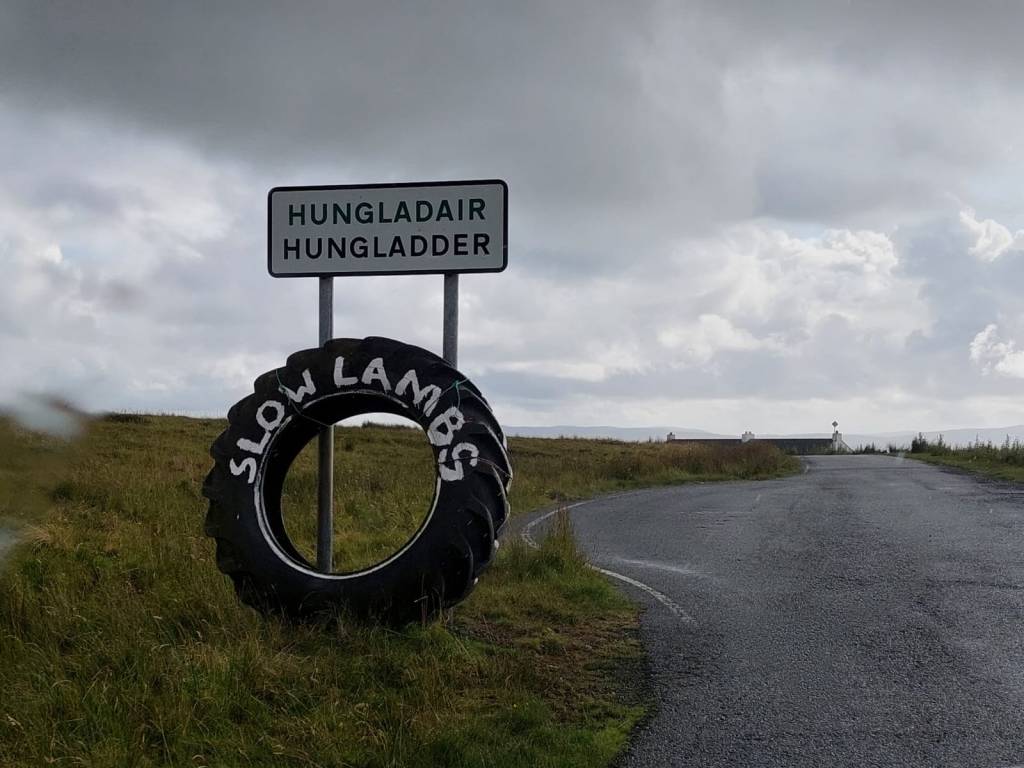 Tienposkessa nimikylttiin nojaileva traktorinrengas, johon on kirjoitettu valkoisella maalilla "slow lambs".