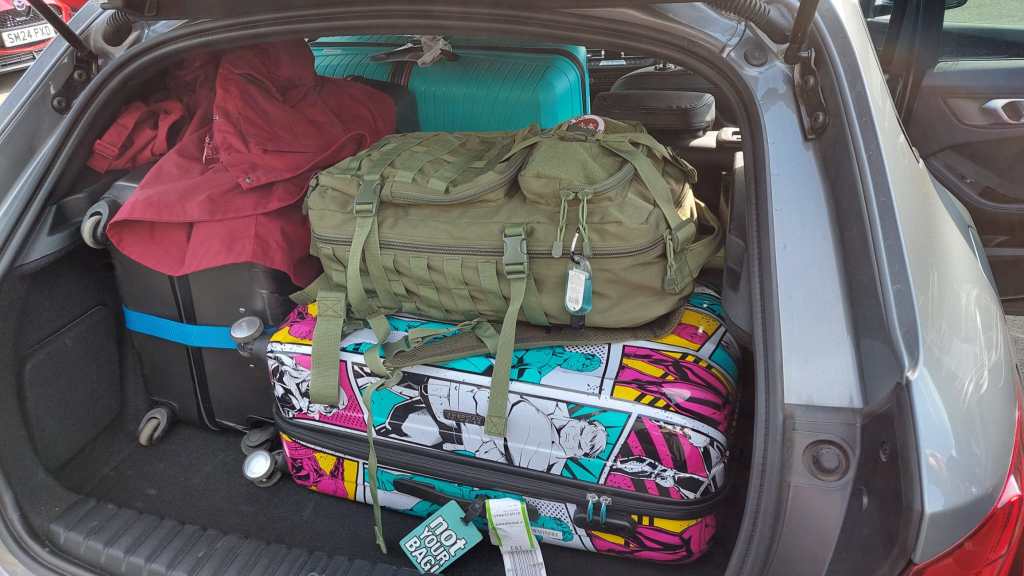 Kuva täyteen ahdetusta takakontista, jossa on kaksi matkalaukkua ja iso reppu. Kolmas matkalaukku näkyy taustalla: se ei ole enää takakontissa, vaan kaadettujen takapenkkien päällä. Yhden laukun päälle on heitetty punainen takki.