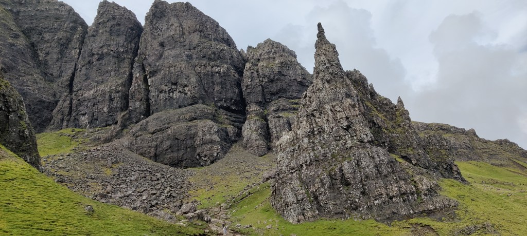 Kuvassa isojen kallioiden väliin jäävä kivinen rinne. Taivas on harmaan pilvinen. Rinne viherää kivikkojen alta.
