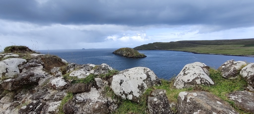 Kivireunuksen takaa otettu kuva merenlahdesta, jolla näkyy yksinäinen kalliosaari. Sen takana näkyy rannikkoa. Taivas on pilvinen.
