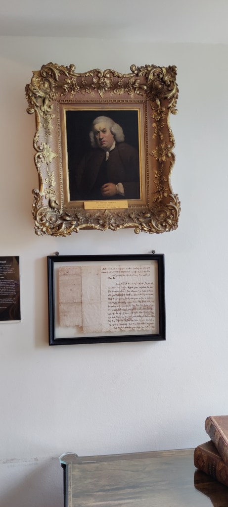 Kultaisiin, paksuihin kehyksiin laitettu maalaus hämmentyneen näköisestä miehestä, jolla on vaalea peruukki.