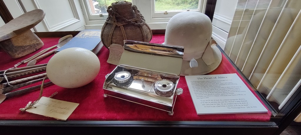 Vitriinikaappi, jossa jonkinlainen ääninauhalaite, hellekypärä, vesipullo ja strutsinmuna.