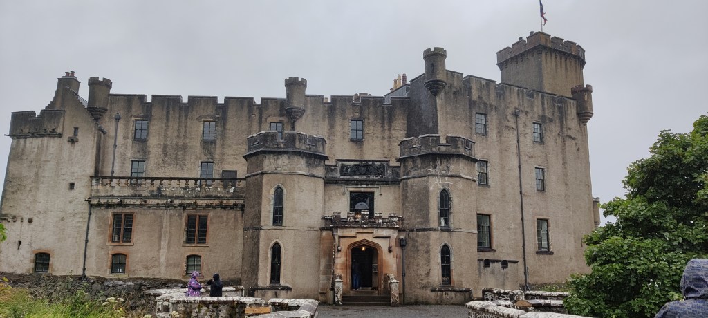 Kivinen, hiekkakiven värinen linna, jossa yksi iso torni oikeassa reunassa. Edessä linnan ovi, jonka kummallakin puolella pyöreät porttitornit. Useita, neliskanttisia ikkunoita. Kivinen, matala muuri ja harmaa taivas.Tornin huipulla liehuu jonkinlainen lippu.