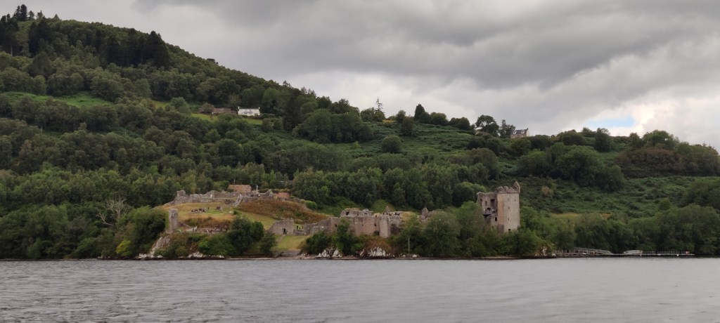 Rannalla erottuvan linnan rauniot, Taustalla metsäinen, kumpuileva maasto.