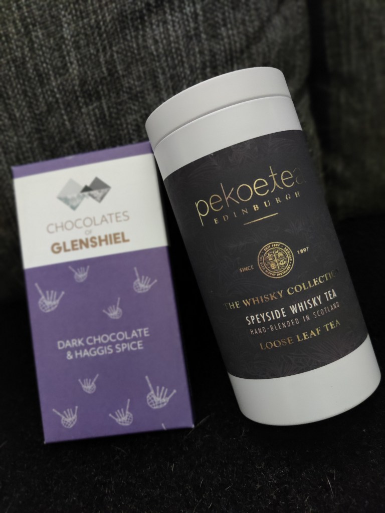 Violetissa pahvipakkauksessa olevaa, haggiksen makuista tummaa suklaata ja vieressä purkki edinburghilaista viskiteetä.