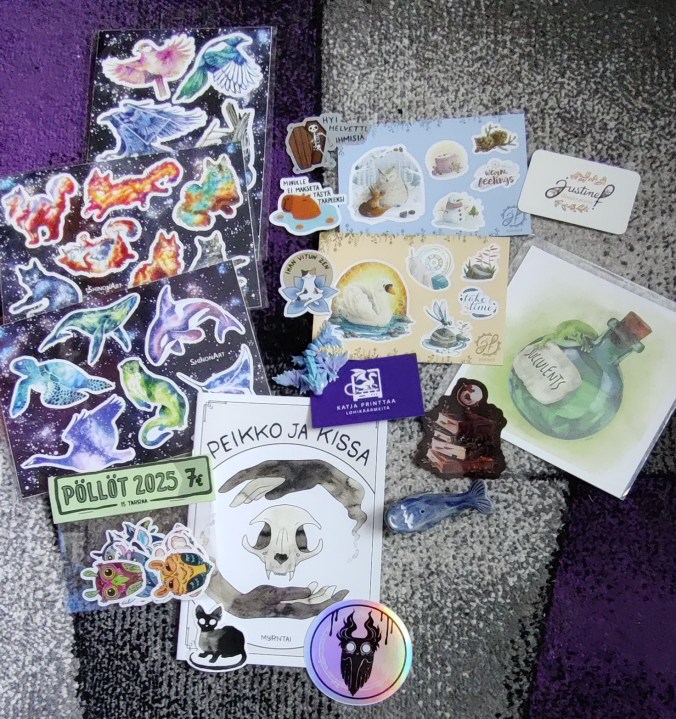 Lattialle levitelty kasa tarroja, joiden joukossa on erilaisia värikkäitä eläimiä, kuten kissoja, lintuja ja pöllöjä, vitsitarroja, kuten "hyi helvetti, ihmisiä". Mukana on myös Peikko ja kissa -niminen zine, pieni taideprintti vihreän pullon päällä kiipeilevästä gekosta ja pieni, savesta tehty sininen valas.