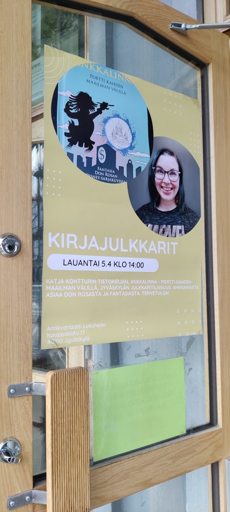 Ovessa oleva iso mainosjuliste, jossa on kuva kirjani kannesta sekä minusta. Teksti mainostaa julkkareita.