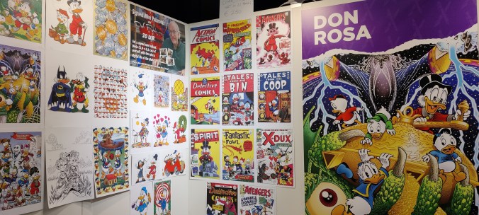 Erikoislähikuva kojun nurkasta. Seinät ovat täynnä Don Rosan piirtämiä Aku- ja Roope-teemaisia kuvia. Mukana on myös parodiaversioita vanhoista sarjakuvalehtien numeroista, kuten Action Comicsin ja Detective Comicsin ensimmäisistä numeroista. Oikeassa reunassa on jättimäinen kuva Sammon salaisuudesta.