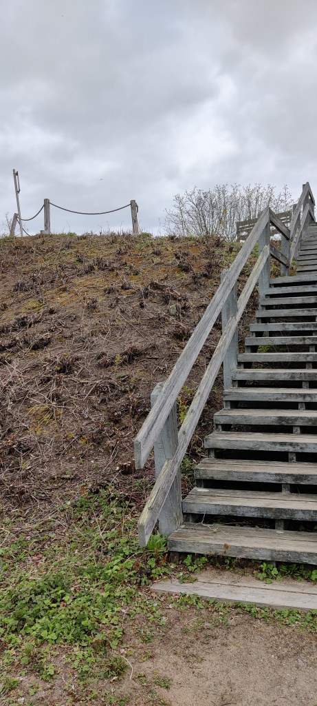 Puiset portaat johtavat pienelle kukkulalle, jonka päällä näkyy puisia tolppia, joita yhdistää toisiinsa köysi.