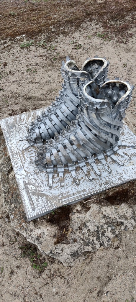 Lähikuva veistoksesta, jossa saappaiden yli kulkevat "remmit" naulaavat ne kiinno koristeelliseen alustaan.