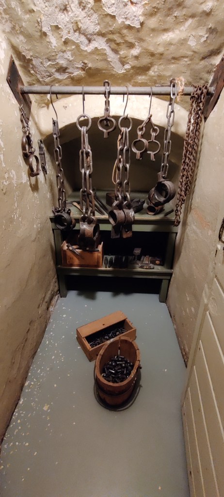 Pieni syvennys, jossa roikkuu useita metallisia kahleita, kettinkejä ja muita vanhoja tykötarpeita ihmisen kahlitsemiseen.