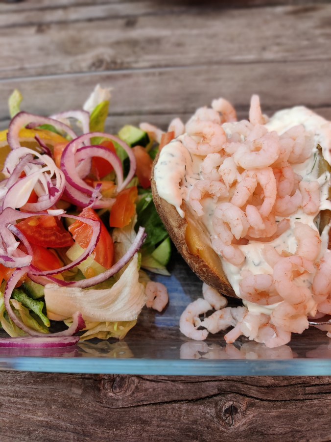 Erikoislähikuvassa vihersalaatti, jonka vieressä katkaravuilla täytetty uuniperuna.