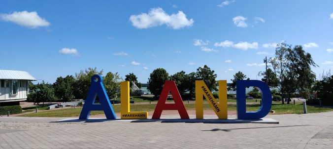 Sinisellä, keltaisella ja punaisella värillä maalattu iso ÅLAND-kyltti.