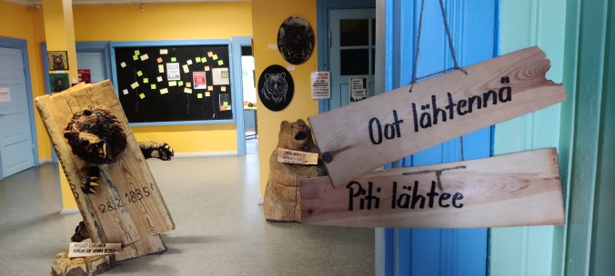 Näyttelyn aulassa karhupatsas ja kaksi kylttiä: "Oot lähtennä" ja "Piti lähtee".