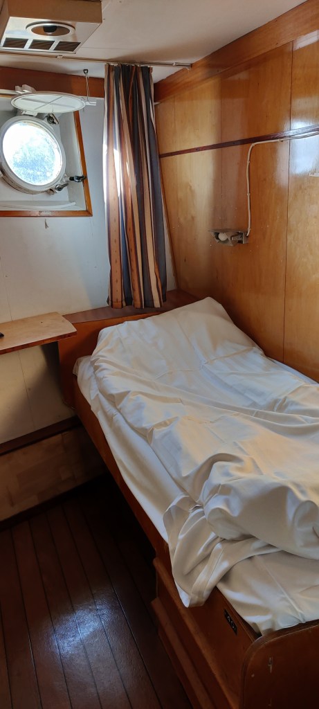 Pieni hytti: kuvassa sänky ja takaseinällä pyöreä ikkuna.