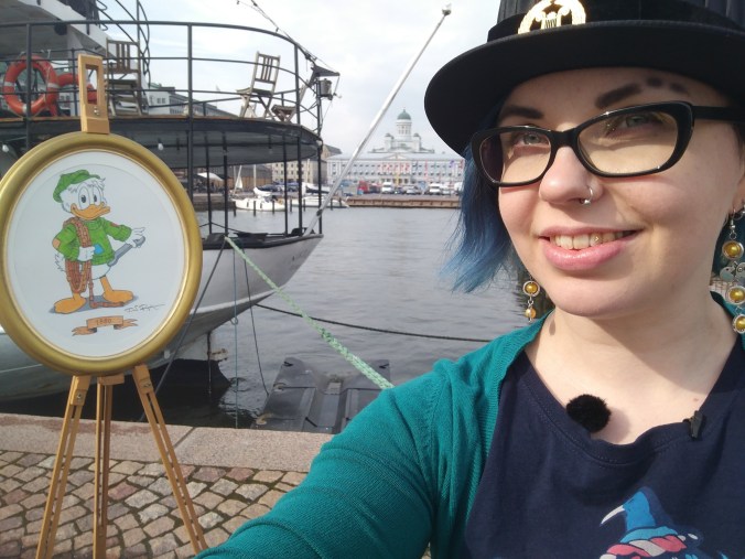 Satamassa otettu selfie Katjasta, jolla on tohtorinhattu päässä. Taustalla näkyy Don Rosan piirtämä potretti nuoresta Roope Ankasta.